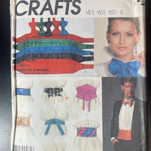 May include: McCall's Crafts pattern featuring cummerbund designs. The cover displays various cummerbund styles in colors like red, green, and blue, along with a woman and a man modeling the accessories. The text reads "TIE IT... BOUCLER, A NOUER..."