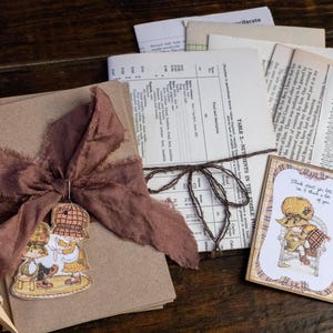 May include: A brown paper package tied with twine and a brown fabric bow. The package is decorated with a vintage illustration of two girls in dresses. A card with the text "Think about you lots, and I think a lot of you" is on the table next to the package.