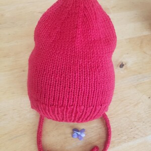 May include: A red knitted hat with a pointed top and a long tie. The hat is made of a soft, warm yarn and has a simple, classic design.