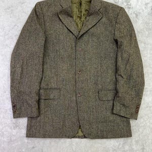 May include: A brown tweed blazer featuring a textured speckled pattern, a notched lapel, and three front buttons. The jacket includes two flap pockets at the waist, four buttons on each sleeve cuff, and a solid olive green interior lining.