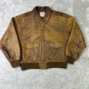 Puede incluir: Chaqueta de cuero marrón con un aspecto desgastado y envejecido. Presenta cuello, dos bolsillos delanteros y puños y dobladillo de canalé. El cuero tiene un aspecto moteado y envejecido.