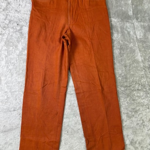 May include: A pair of orange pants with a straight leg design. The pants have a button and zipper closure, belt loops, and front and back pockets. The fabric appears to be a medium-weight material.