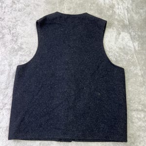 May include: A sleeveless vest in a dark charcoal gray color with a textured, felted appearance. The garment features a rounded neckline, wide arm openings, and a straight hemline, showcasing a simple, solid-colored design without any visible closures.