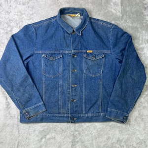 Puede incluir: Chaqueta vaquera azul vintage con cierre de botones, dos bolsillos en el pecho y dos bolsillos laterales. La chaqueta tiene un cuello clásico y mangas largas. El denim tiene un aspecto desgastado, lo que sugiere que es un artículo de segunda mano.
