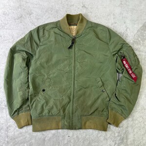 Puede incluir: Chaqueta bomber verde oliva con cuello, puños y dobladillo acanalados. Cuenta con cierre de cremallera, dos bolsillos delanteros y una etiqueta roja "REMOVE BEFORE FLIGHT" en la manga izquierda. Diseño clásico de inspiración militar.
