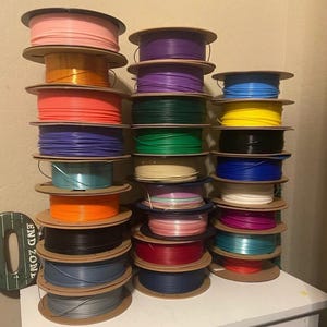 Puede incluir: Una colecci&oacute;n de bobinas de filamento para impresora 3D de colores, incluyendo rosa, naranja, morado, verde y azul. Las bobinas est&aacute;n apiladas, mostrando una variedad de materiales de impresi&oacute;n.