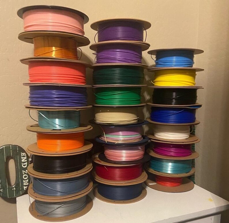 Puede incluir: Una colecci&oacute;n de bobinas de filamento para impresora 3D de colores, incluyendo rosa, naranja, morado, verde y azul. Las bobinas est&aacute;n apiladas, mostrando una variedad de materiales de impresi&oacute;n.