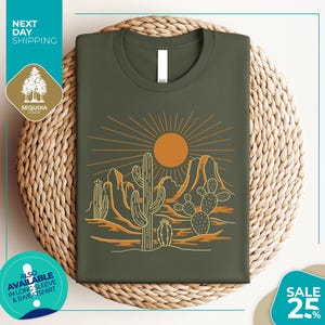 a green t-shirt with a desert landscape design, including cacti and mountains, along with a sun illustration. The t-shirt is displayed on a woven basket, and there are various texts and logos surrounding the image.