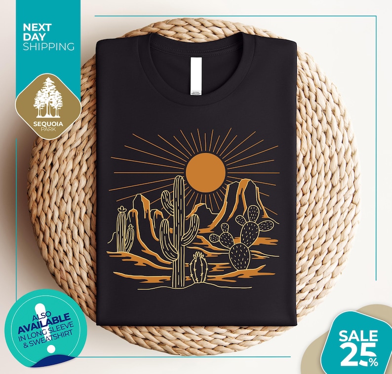 a black t-shirt with a graphic design depicting a desert landscape with cacti and mountains, along with a sun and rays. The t-shirt is displayed on a woven mat, and there are various texts and logos surrounding the image.