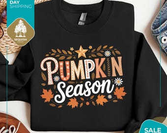 May include: Black sweatshirt with the words "PUMPKIN Season" in a fall-themed design. The design includes orange leaves, a gold star, and white flowers. The sweatshirt is a Gildan brand.