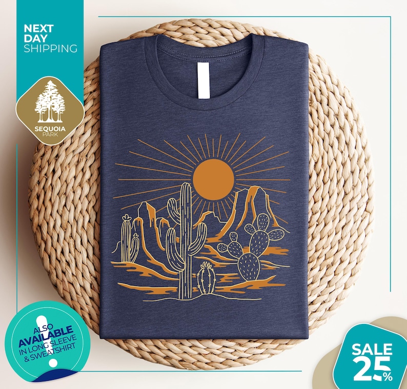 a blue t-shirt with a desert landscape design, including cacti and mountains, along with a sun and rays. The t-shirt is displayed on a woven mat, and there are various texts and logos surrounding the image.