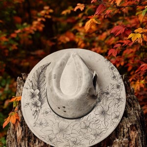 THE FEATHER is a beautiful gray vegan suede fedora wide brim hat that a pyrography tool was used to hand-burn the feather and flowers.