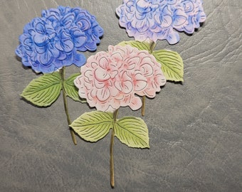May include: Three paper hydrangea flowers, one pink, two blue, with green leaves and stems.