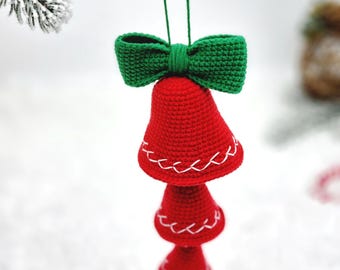 May include: A handmade Christmas ornament featuring three red crocheted bells with white stitching, topped with a green crocheted bow. The ornament is suspended from a green string, perfect for holiday decor.