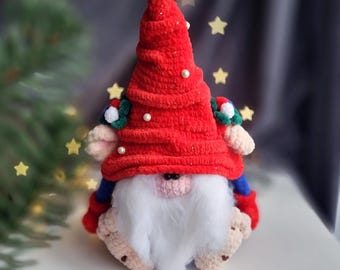 May include: A red crocheted gnome with a white beard and a red hat decorated with white pearls. The gnome is sitting on a white surface.