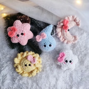 Puede incluir: Cinco juguetes de peluche tejidos a crochet en forma de estrella, gota de lluvia, media luna, sol y nube. Cada juguete tiene un lazo rosa y una cara linda.