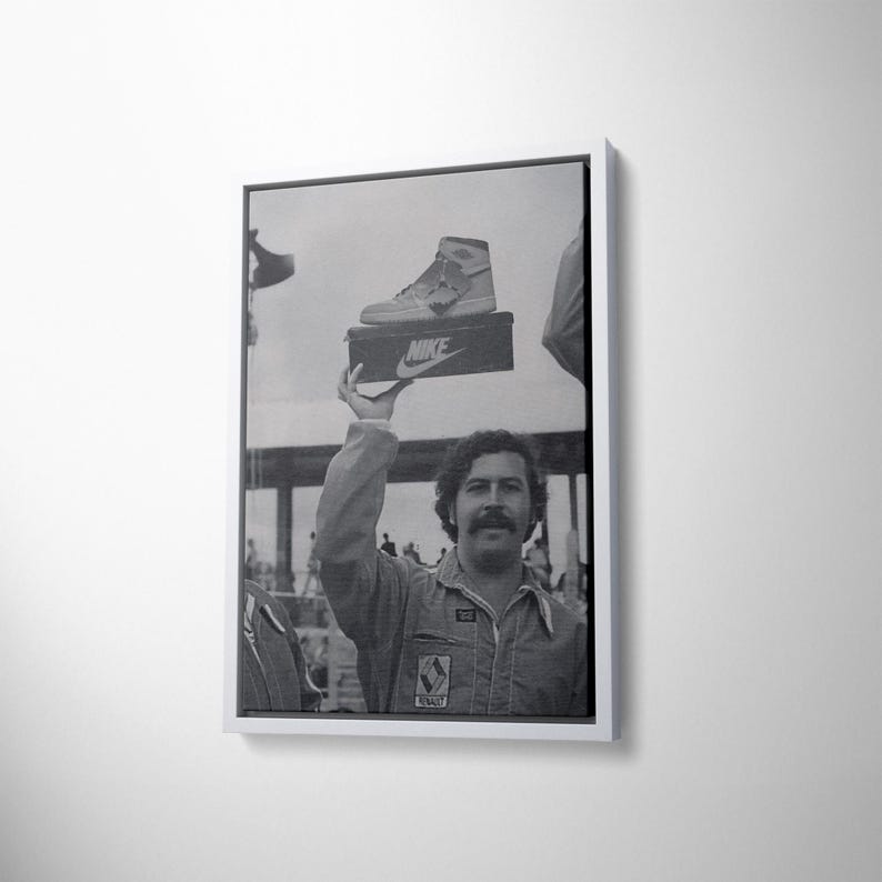 May include: Monochrome framed print showing a man holding a Nike shoe box. The box displays the Nike logo. The man, wearing a jumpsuit, has a moustache. The image is a vintage photograph.