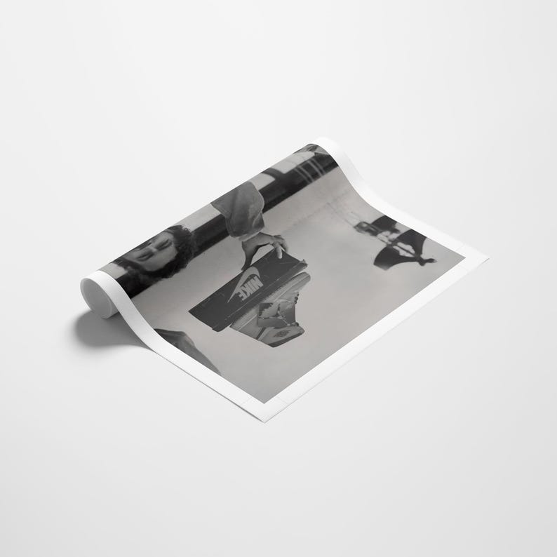 May include: Monochrome image of a person holding a Nike shoe box and a sneaker. The box is black with a white Nike logo. The sneaker is light-colored, possibly beige or cream.