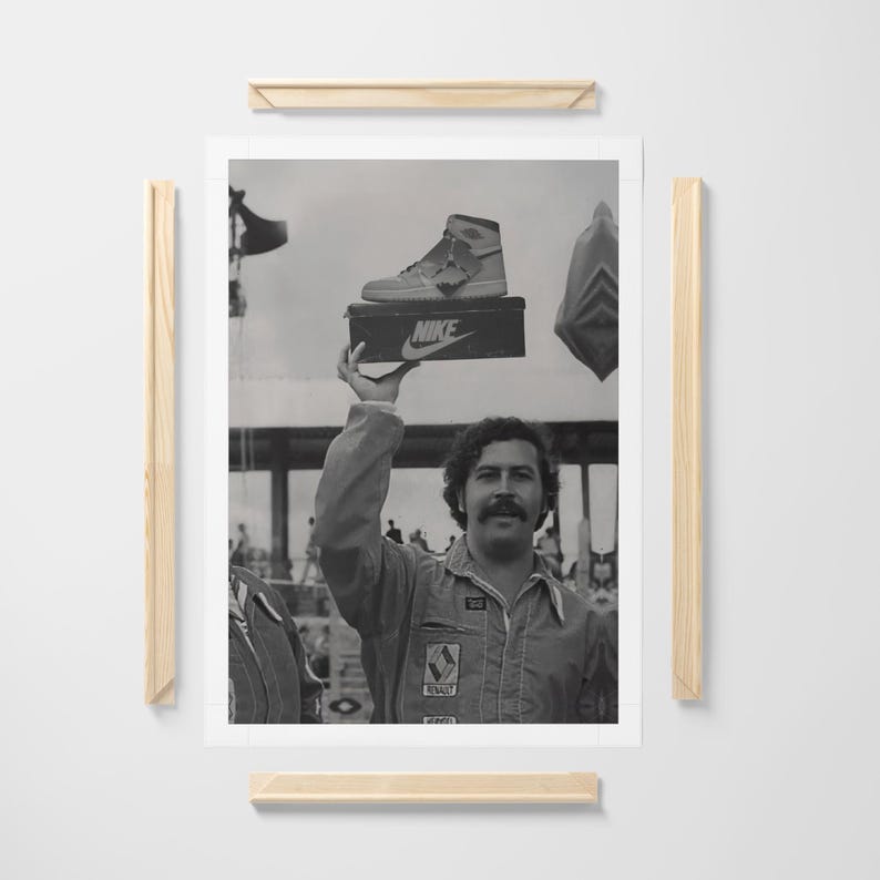 May include: Monochrome framed print showing a man holding a Nike shoe box with a high-top trainer. The man wears a jumpsuit and has a moustache. A crowd of people is visible in the background.