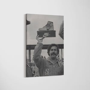 May include: Monochrome canvas print showing a man holding a Nike shoebox with a high-top trainer. The man wears a jumpsuit and has a moustache. The Nike logo is visible on the shoebox.