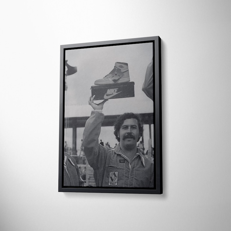 May include: Black and white framed print showing a man holding a Nike shoe box with a high-top trainer on top. The image is a vintage photograph with a black frame.