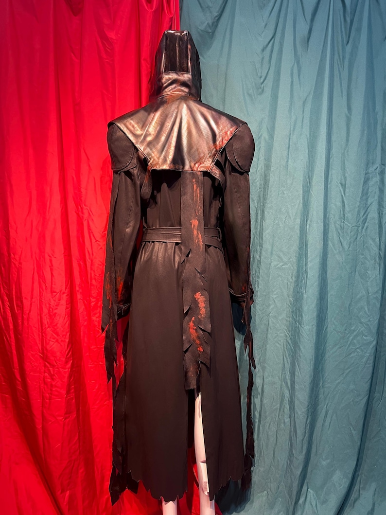 May include: A black hooded cloak with a leather-like appearance, featuring red accents and a belt. The cloak has a long, flowing design with jagged edges and is displayed against a red and teal backdrop.