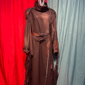 May include: A black Scream costume with a white mask. The costume features a long, dark robe with tattered edges and a belt. Red accents are visible on the belt and sleeves. The mask has a wide open mouth.