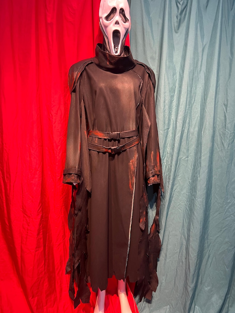 May include: A black Scream costume with a white mask. The costume features a long, dark robe with tattered edges and a belt. Red accents are visible on the belt and sleeves. The mask has a wide open mouth.