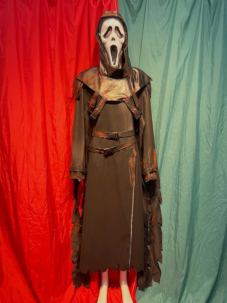 May include: A dark brown Ghostface costume with a white mask, hood, and long robe. The costume features a leather-like chest piece with straps and a belt. The robe has jagged edges and a zipper down the front. The background is red and teal.