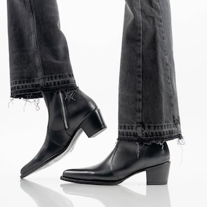 Puede incluir: Botines de cuero negro con punta afilada, tacón de bloque y cierre de cremallera lateral en tono plateado. Los botines se llevan con vaqueros de mezclilla gris oscuro con un dobladillo deshilachado y corte crudo que cae sobre el tobillo.