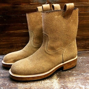 May include: A pair of tan suede mid-calf boots featuring a rounded toe, a pull tab at the top of the shaft, and a stacked wooden heel with a light-colored welt. The boots have a textured, fuzzy surface and a clean, simple construction.