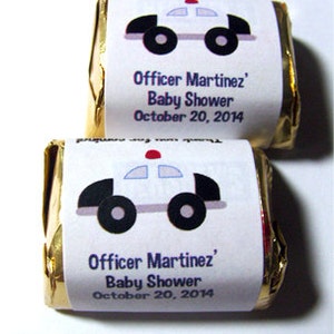 Pode incluir: Duas barras de chocolate embrulhadas em papel alum&iacute;nio dourado com etiquetas brancas. As etiquetas apresentam um carro de pol&iacute;cia de desenho animado com uma luz vermelha no topo e o texto "Officer Martinez' Baby Shower October 20, 2014".