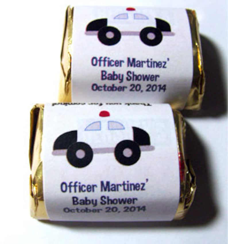 Pode incluir: Duas barras de chocolate embrulhadas em papel alum&iacute;nio dourado com etiquetas brancas. As etiquetas apresentam um carro de pol&iacute;cia de desenho animado com uma luz vermelha no topo e o texto "Officer Martinez' Baby Shower October 20, 2014".