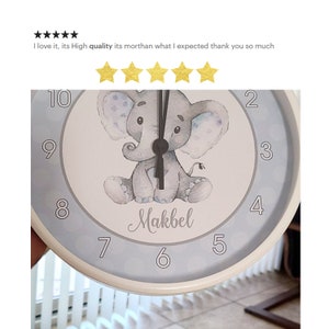 May include: A white and blue round clock with a gray elephant illustration and the name "Makbel" written below. The clock has black hands and numbers 1 through 12.