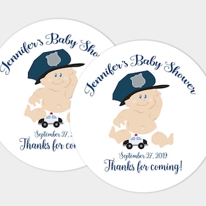 May include: Two round white stickers with a cartoon baby wearing a blue police hat and holding a toy police car. The text on the stickers says "Jennifer's Baby Shower" and "September 27, 2019 Thanks for coming!"
