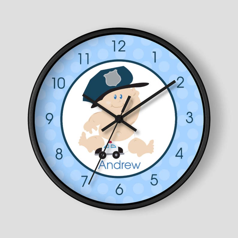 May include: A blue and white clock with a cartoon baby wearing a police hat and holding a toy police car. The clock face has a white background with blue polka dots and black numbers. The clock face also has the name "Andrew" printed on it.