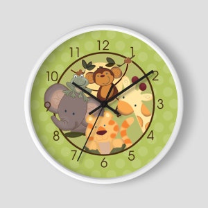 May include: A white clock with a green face and brown numbers. The clock features a cartoon elephant, monkey, giraffe, tiger, and frog. The clock face has a green background with white polka dots.