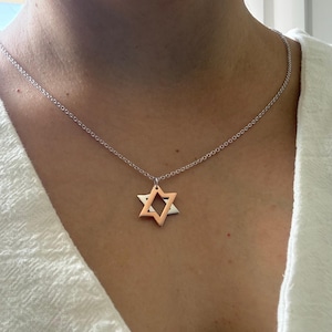 May include: A silver-toned chain necklace featuring a dual-layered Star of David pendant. The front layer of the star is rose gold-toned, while the back layer is silver-toned, creating a layered effect suspended from a delicate link chain.