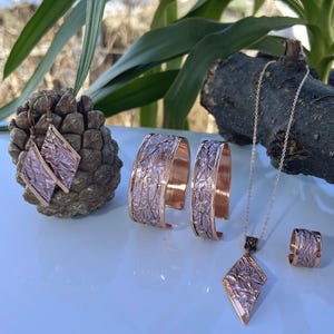 Op de afbeelding: Een set roségouden sieraden met een ketting, oorbellen, een ring en twee armbanden. De sieraden zijn gemaakt van koper en hebben een getextureerde, gehamerde afwerking.