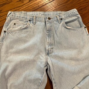 May include: Light wash denim jeans with a classic five-pocket design. The jeans feature a button and zipper closure, belt loops, and rivets at the pocket corners. The light blue color is consistent throughout the garment.
