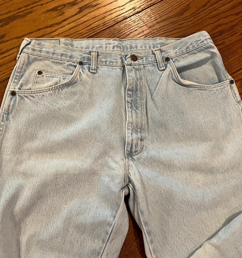 May include: Light wash denim jeans with a classic five-pocket design. The jeans feature a button and zipper closure, belt loops, and rivets at the pocket corners. The light blue color is consistent throughout the garment.