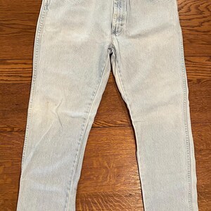 May include: Light blue denim jeans with a classic five-pocket design. The jeans have a straight leg cut and a button and zipper closure. The light wash denim shows subtle fading and wear, giving them a vintage look.