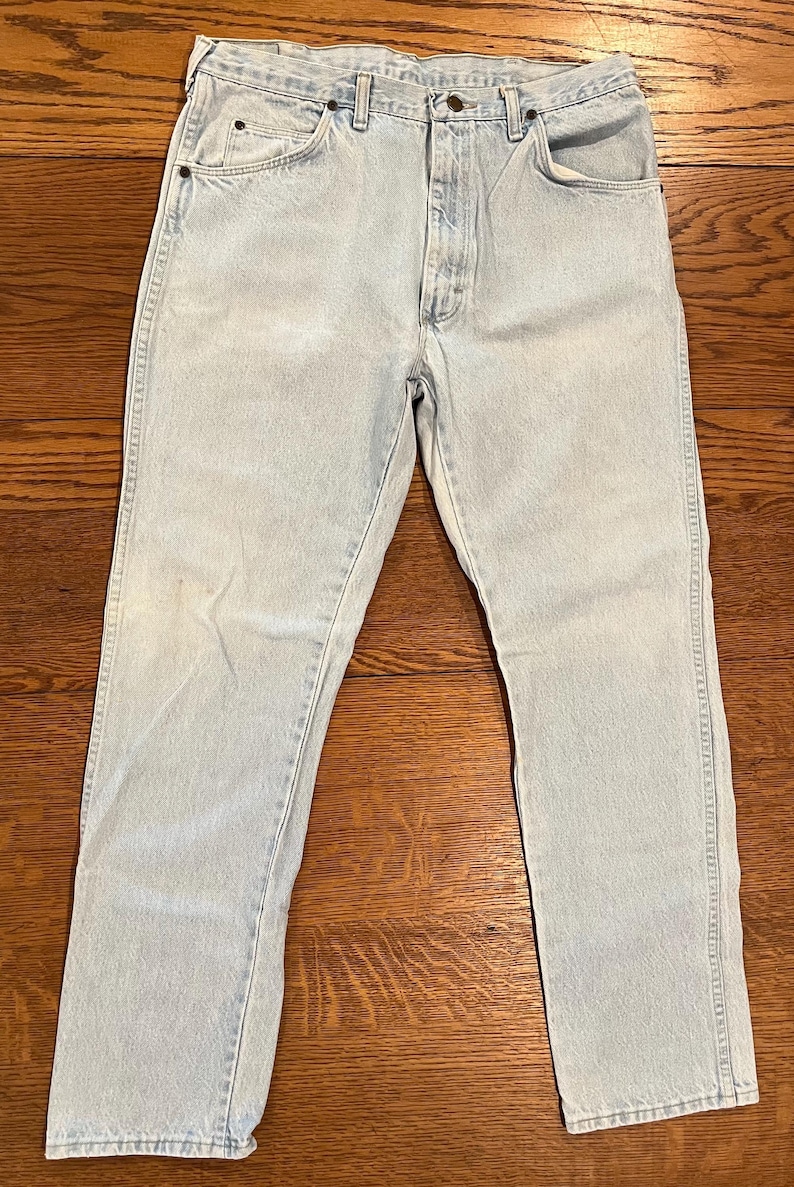May include: Light blue denim jeans with a classic five-pocket design. The jeans have a straight leg cut and a button and zipper closure. The light wash denim shows subtle fading and wear, giving them a vintage look.
