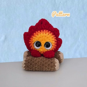 Peut inclure: Un jouet en peluche crocheté en forme de feu de camp avec un centre de flammes rouge et orange, de grands yeux en plastique noir et blanc, et des bûches marron à la base. Le mot Pattern est écrit en blanc avec un contour orange clair.