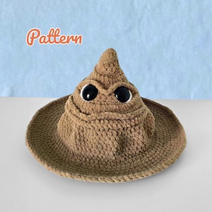 May include: A brown crocheted hat with a pointed top and a wide brim, featuring two large black plastic eyes set into the fabric. The word Pattern is written in orange text above the hat, which has a textured, yarn-based construction.