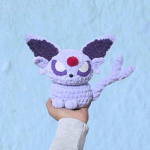 Peut inclure: Une peluche au crochet violet clair avec de grandes oreilles pointues aux sections intérieures violet foncé, un petit pompon rouge sur le front, des yeux blancs aux contours violet foncé et une longue queue fendue en deux parties.