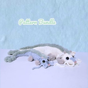 May include: Two crocheted dragon plushies with the text Pattern Bundle above them. The larger dragon is white and sage green, while the smaller one is light blue and sage green. Both feature dark eyes, small horns, and long whiskers.