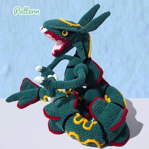 Può includere: Un peluche all'uncinetto a forma di drago serpentiforme in filato verde scuro, con motivi ondulati gialli, accenti rossi lungo i bordi e una bocca rosa con denti bianchi. La parola Pattern è stampata in verde chiaro nell'angolo in alto a sinistra.