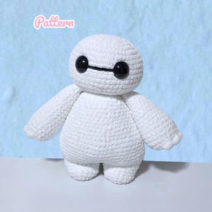 Pode incluir: Um brinquedo de pelúcia de crochê branco com corpo arredondado, membros curtos e dois grandes olhos circulares pretos e lisos conectados por uma linha preta fina. A palavra Pattern está escrita em fonte cursiva rosa claro no canto superior.
