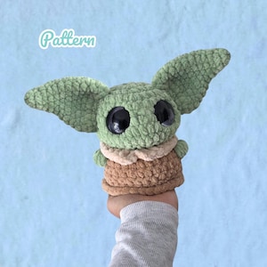 May include: A green crocheted plush toy with large black eyes and oversized pointed ears. The figure wears a tan collar and a brown textured garment. The word Pattern is printed in white script in the upper left corner of the image.